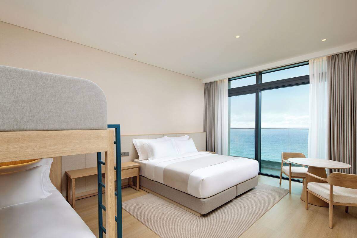 A modern hotel room with a bed, a desk, and a view of the sea.