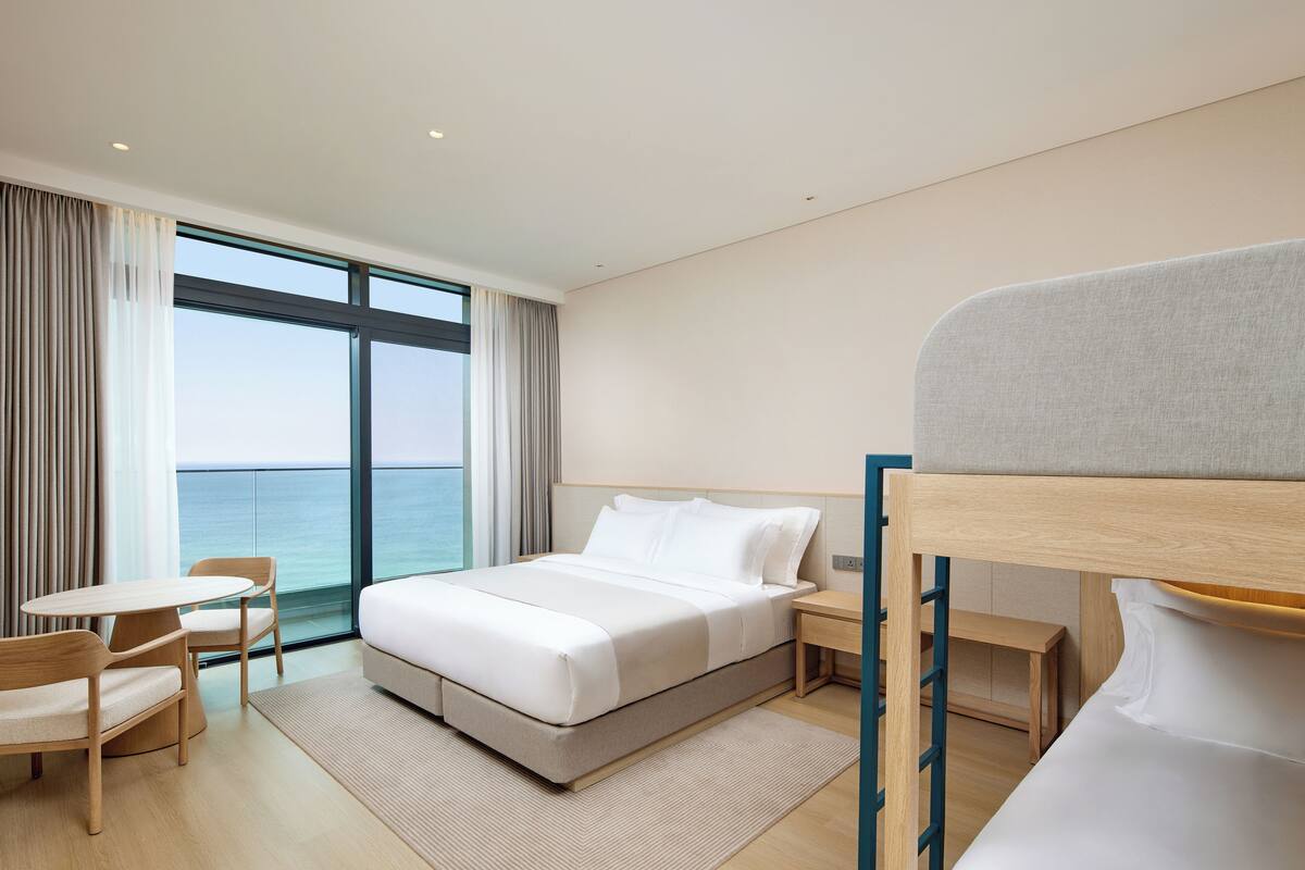 A modern hotel room with a large bed, a desk, and a view of the sea.