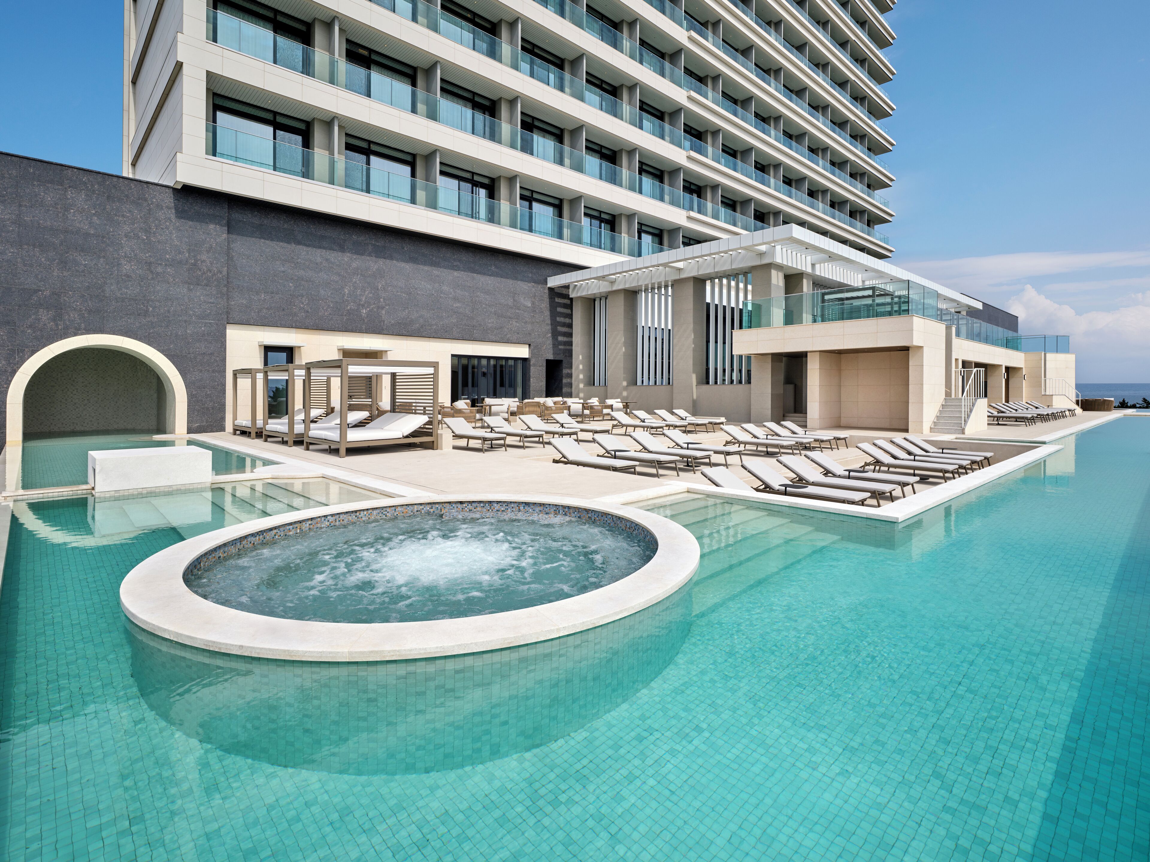 A modern hotel with a rooftop infinity pool, sun loungers, and a spa area.