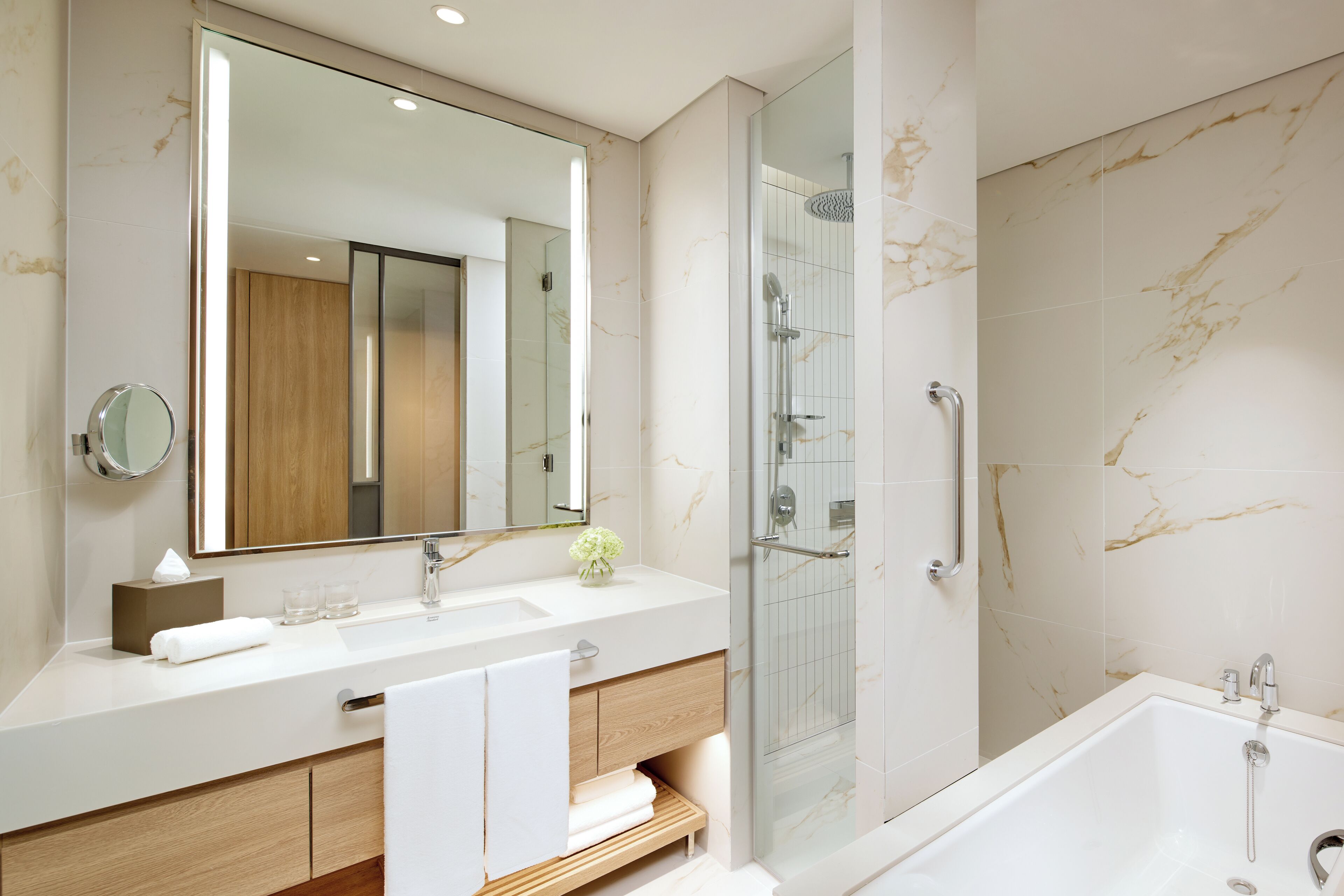 A modern bathroom with a large mirror, two sinks, a shower, and a bathtub.