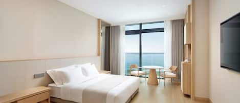 Una habitación de hotel moderna con una cama grande, un escritorio, una silla, una mesita y un televisor.