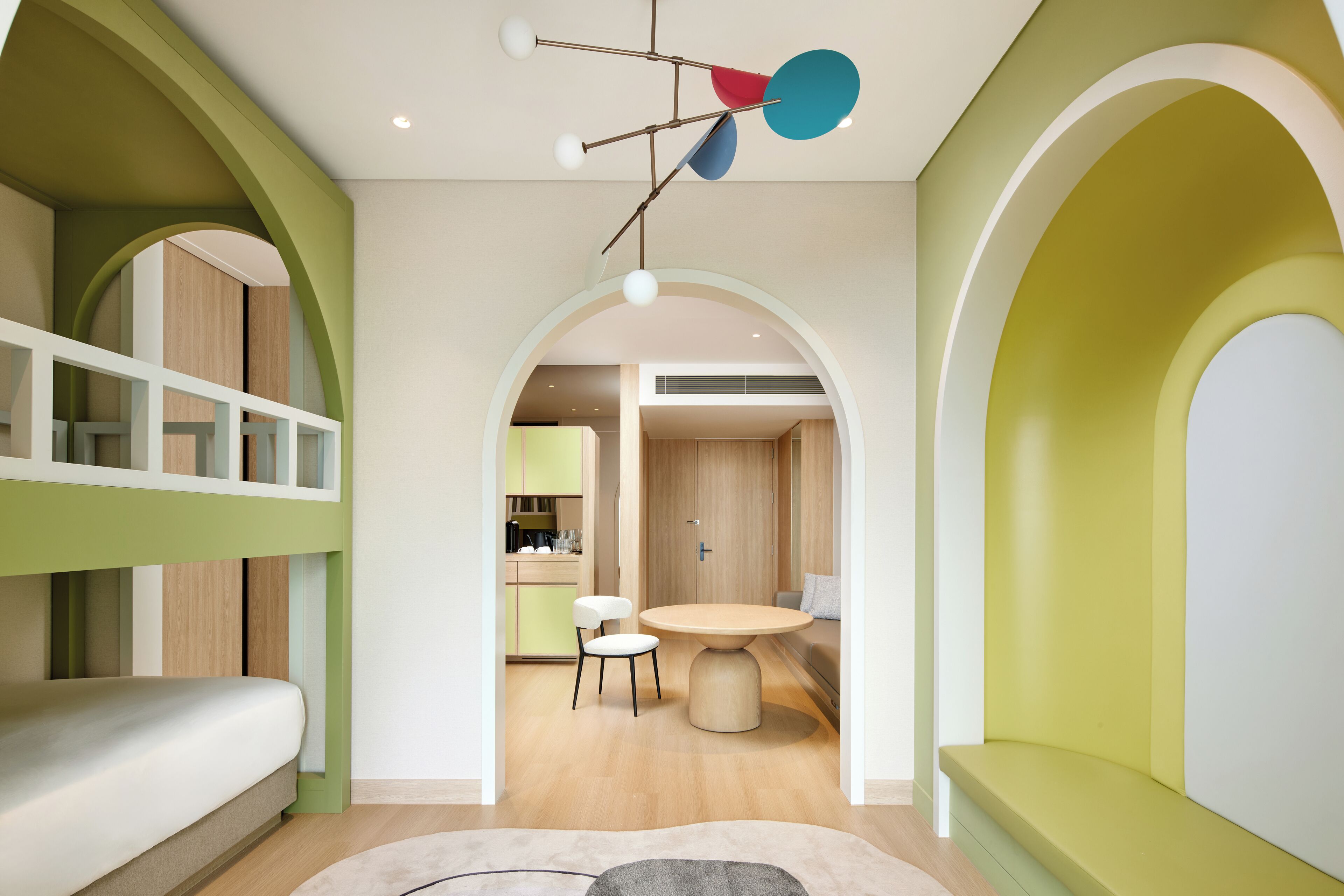 A modern interior with a bunk bed, a round dining table, and a kitchen in the background.