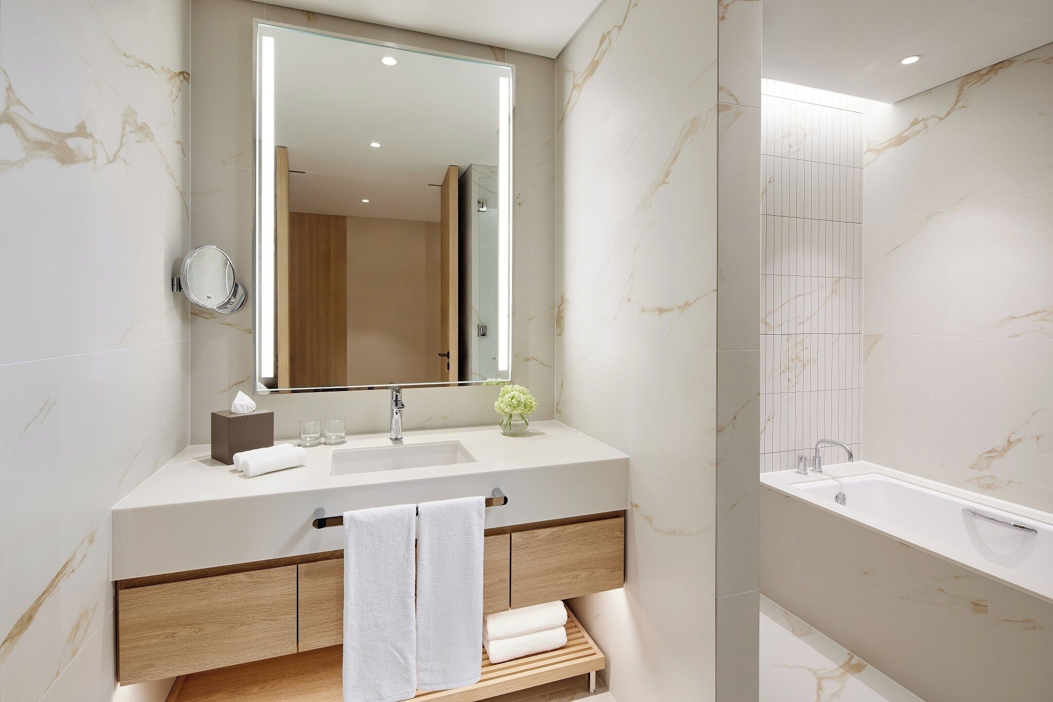 Un baño moderno con un espejo grande, un lavabo, una bañera y muebles de madera.