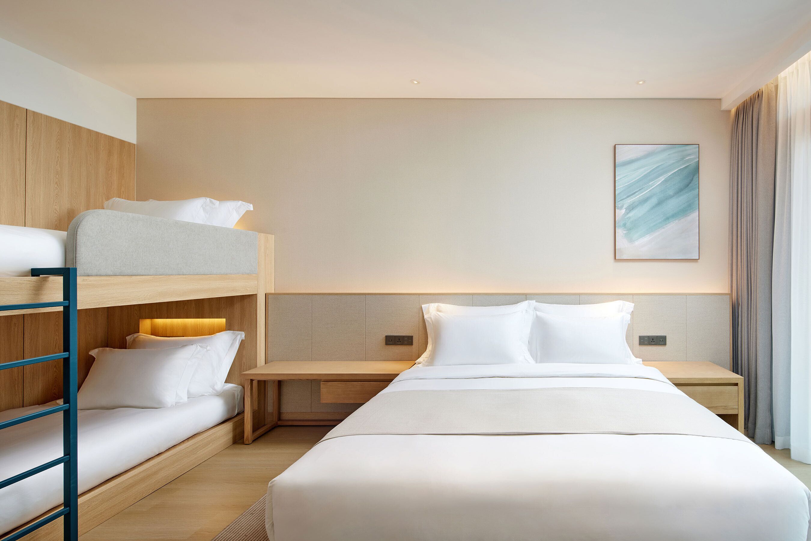 A hotel room with a bunk bed, a single bed, a bedside table, and a wall-mounted artwork.