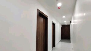 A hallway with white walls, wooden doors, and a tiled floor. - Hotel Blue Shine  (Noida)