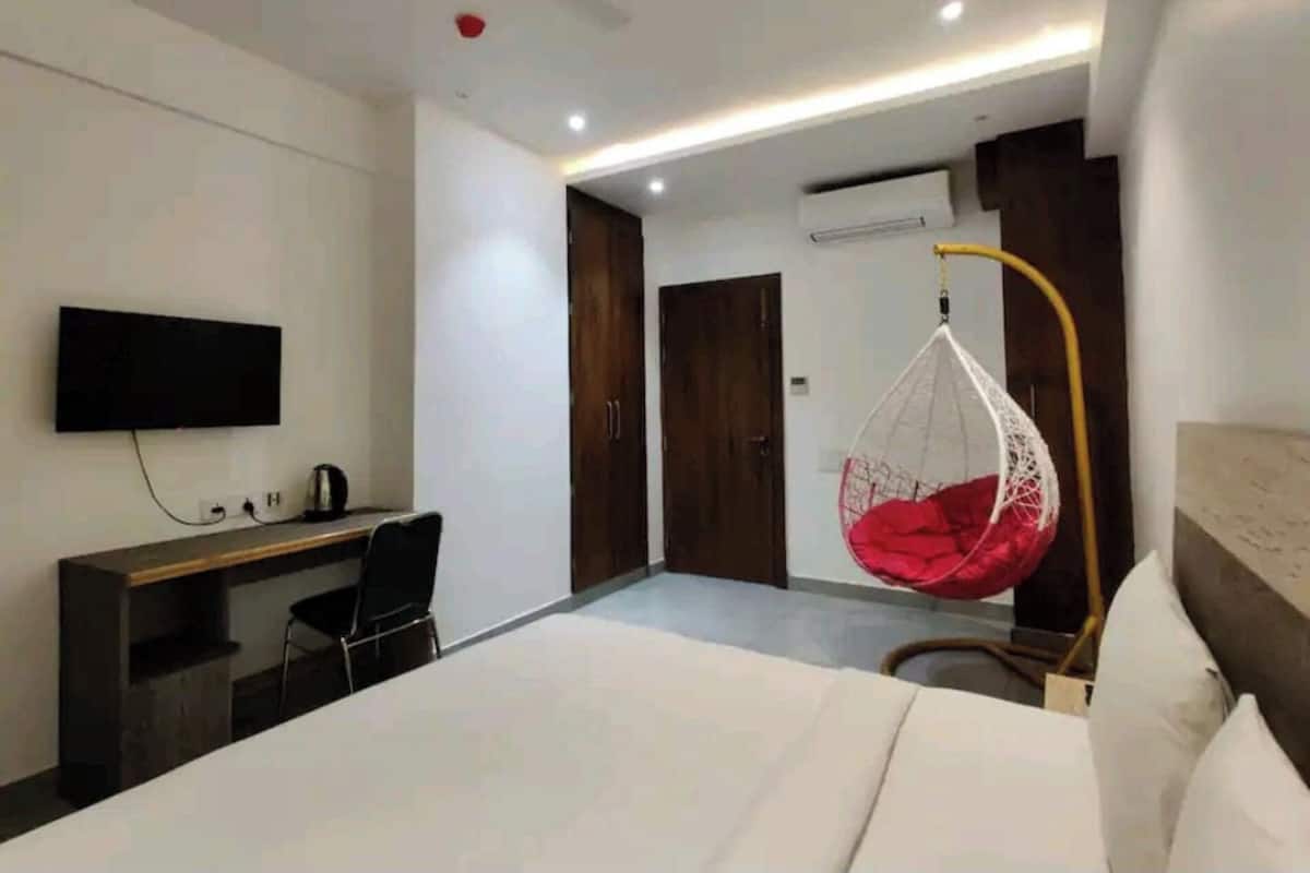 A modern hotel room with a bed, a desk, a chair, a hanging chair, and a TV mounted on the wall.