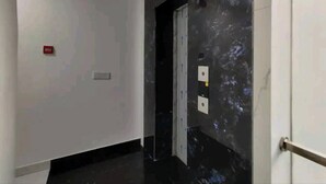 A hallway with a black marble wall, a white door, and a red emergency exit sign. - Hotel Blue Shine  (Noida)