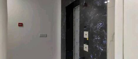 A hallway with a black marble wall, a white door, and a red emergency exit sign.