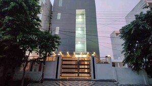 A modern building with a central vertical light feature, a gated entrance, and a patterned pavement. - Hotel Blue Shine  (Noida)