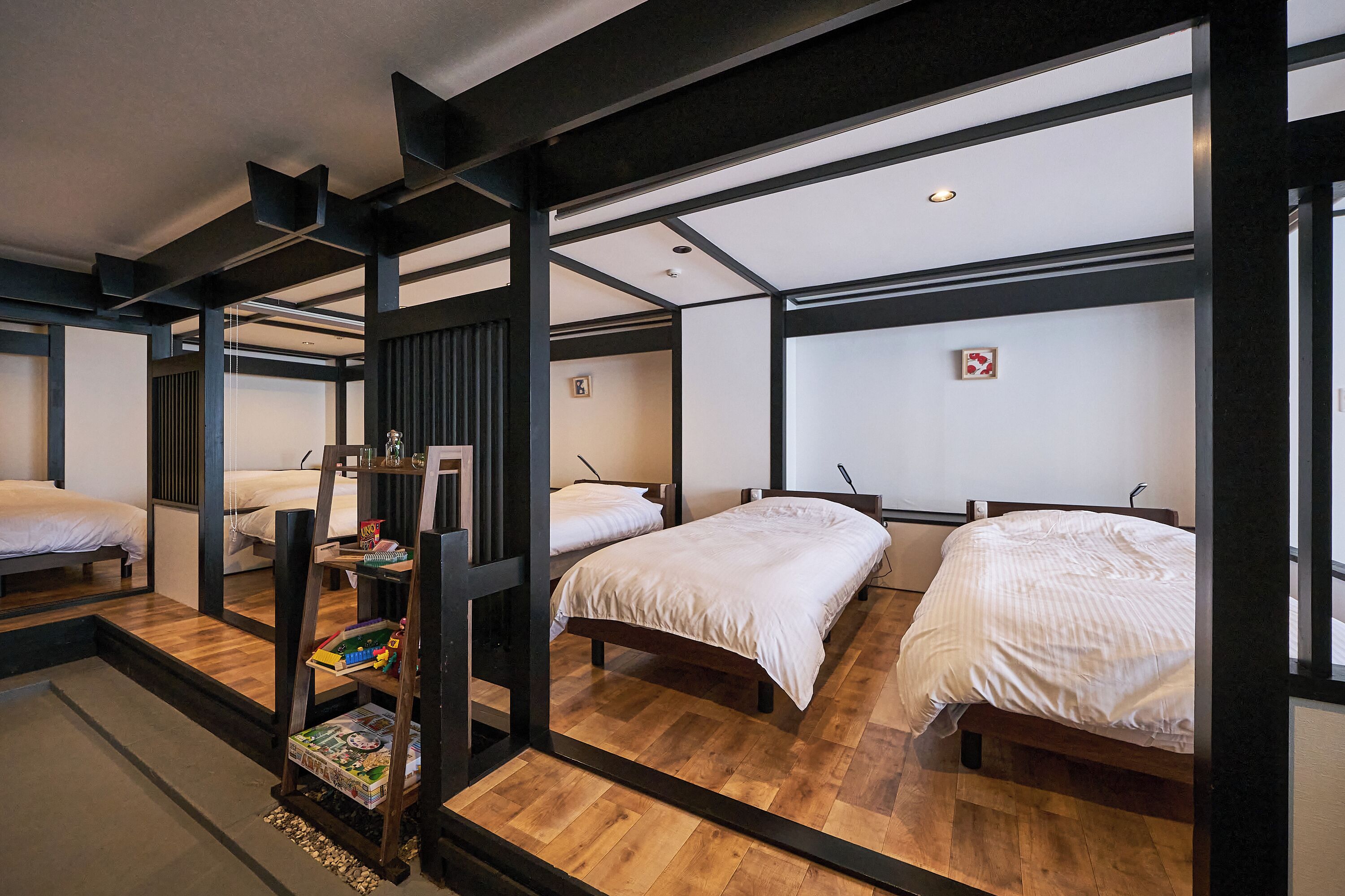 Quarto de hotel com três camas, soalho de madeira e vigas estruturais pretas.
