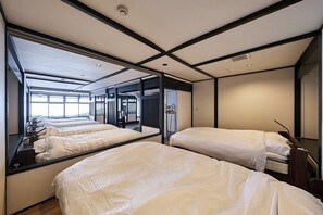 A hotel room with three beds aligned along a wall, a large window providing natural light, and a view of the outside. - ASOBIBA Yoichi Onsenside (Yoichi)