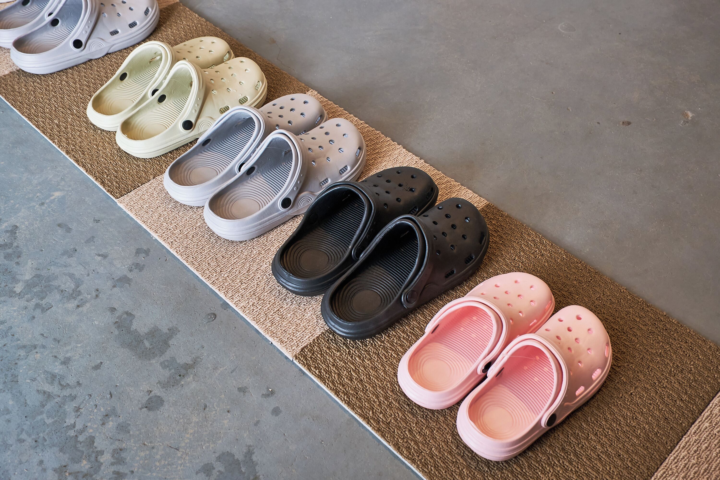 A row of variously colored and sized slippers arranged on a doormat.