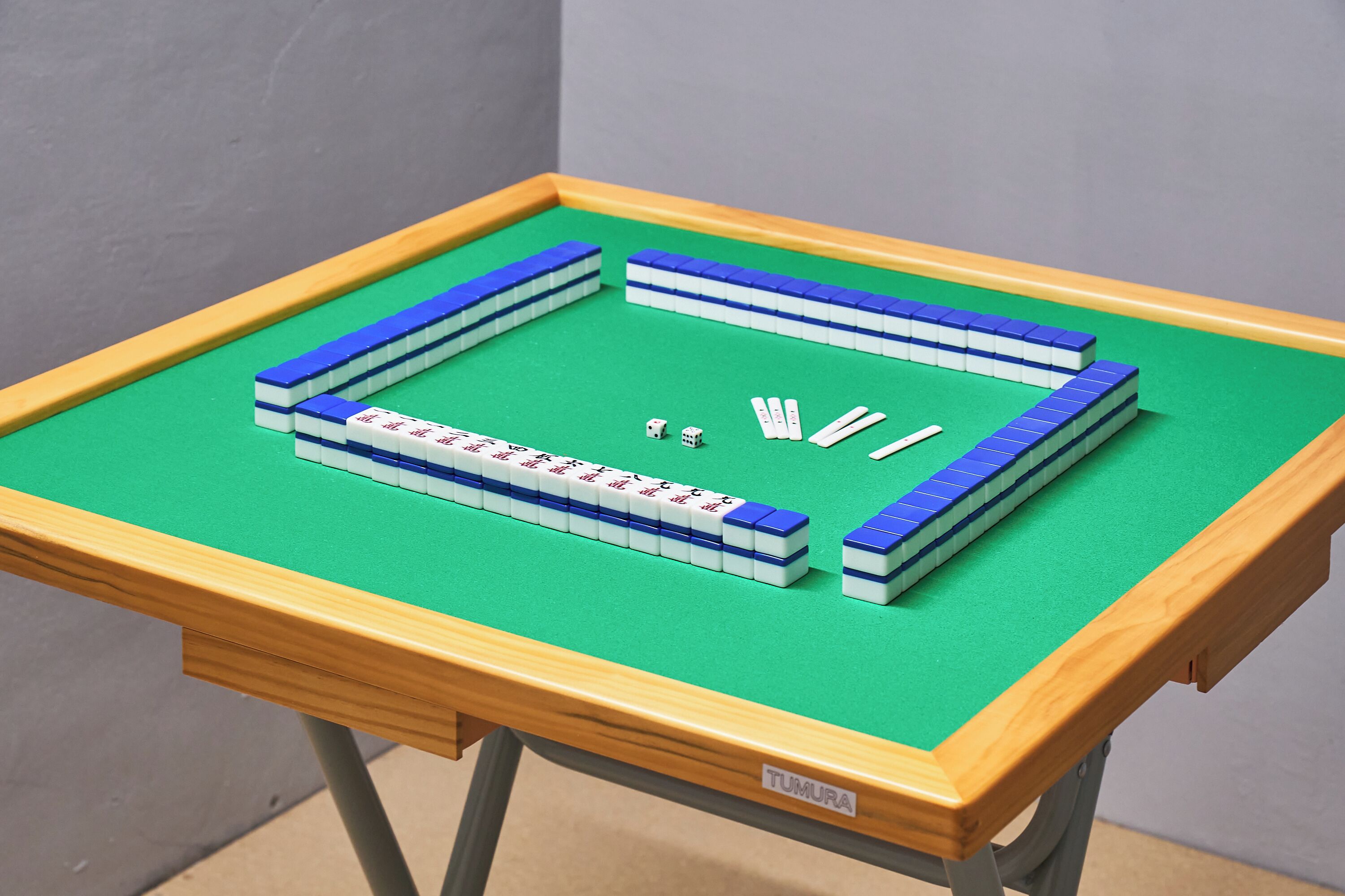 Uma mesa com superfície de feltro verde e moldura de madeira, exibindo um tabuleiro azul e branco e dados.