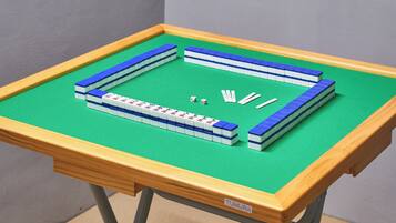 Uma mesa com superfície de feltro verde e moldura de madeira, exibindo um tabuleiro azul e branco e dados.