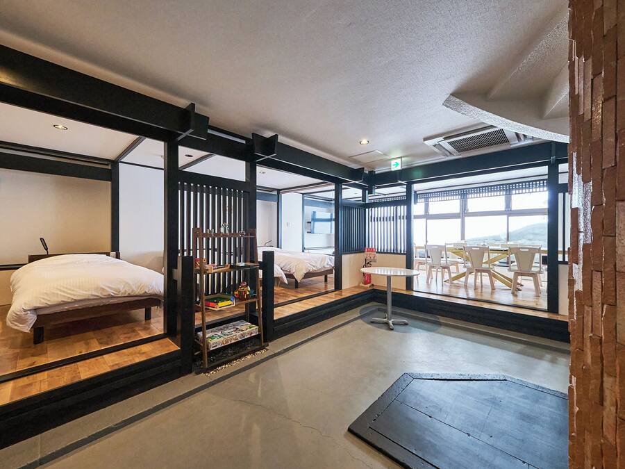 A hotel room with a bed, a small table, and a view of the outside.