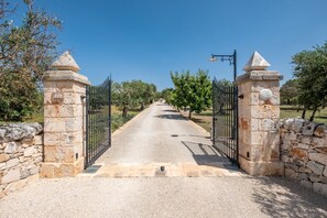 A paved pathway leading through a gate with stone pillars and a metal fence.