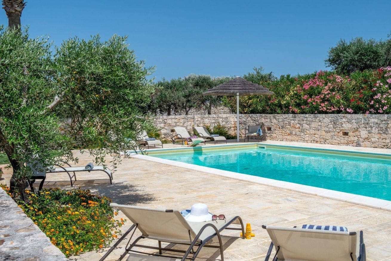 A poolside area with lounge chairs, a stone wall, and a thatched umbrella.