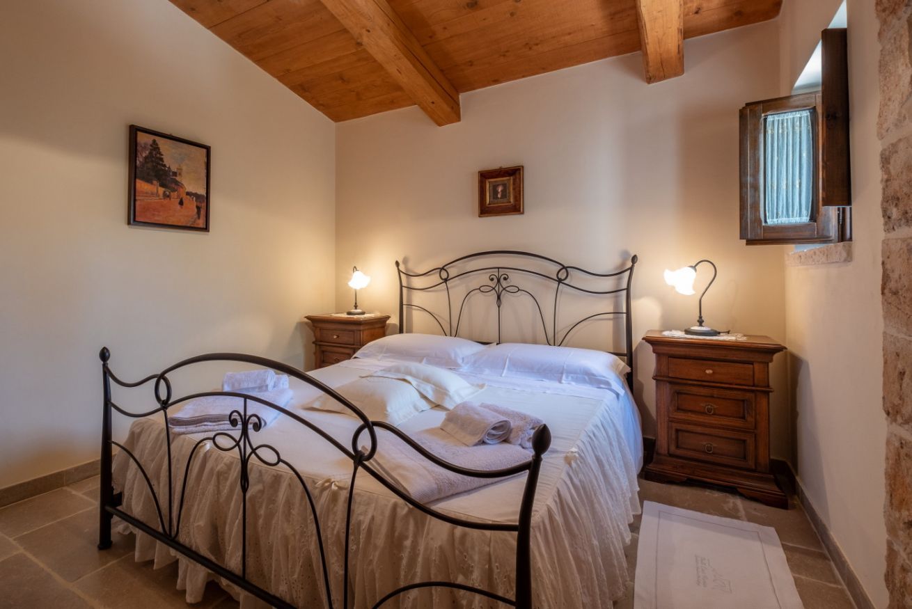 A bedroom with a metal bed frame, two bedside tables, a wooden headboard, and a small window.