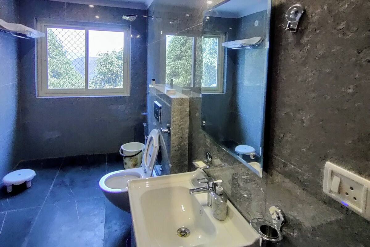 A modern bathroom with a large mirror, a sink, and a toilet. There is a window providing natural light and a view of greenery outside.