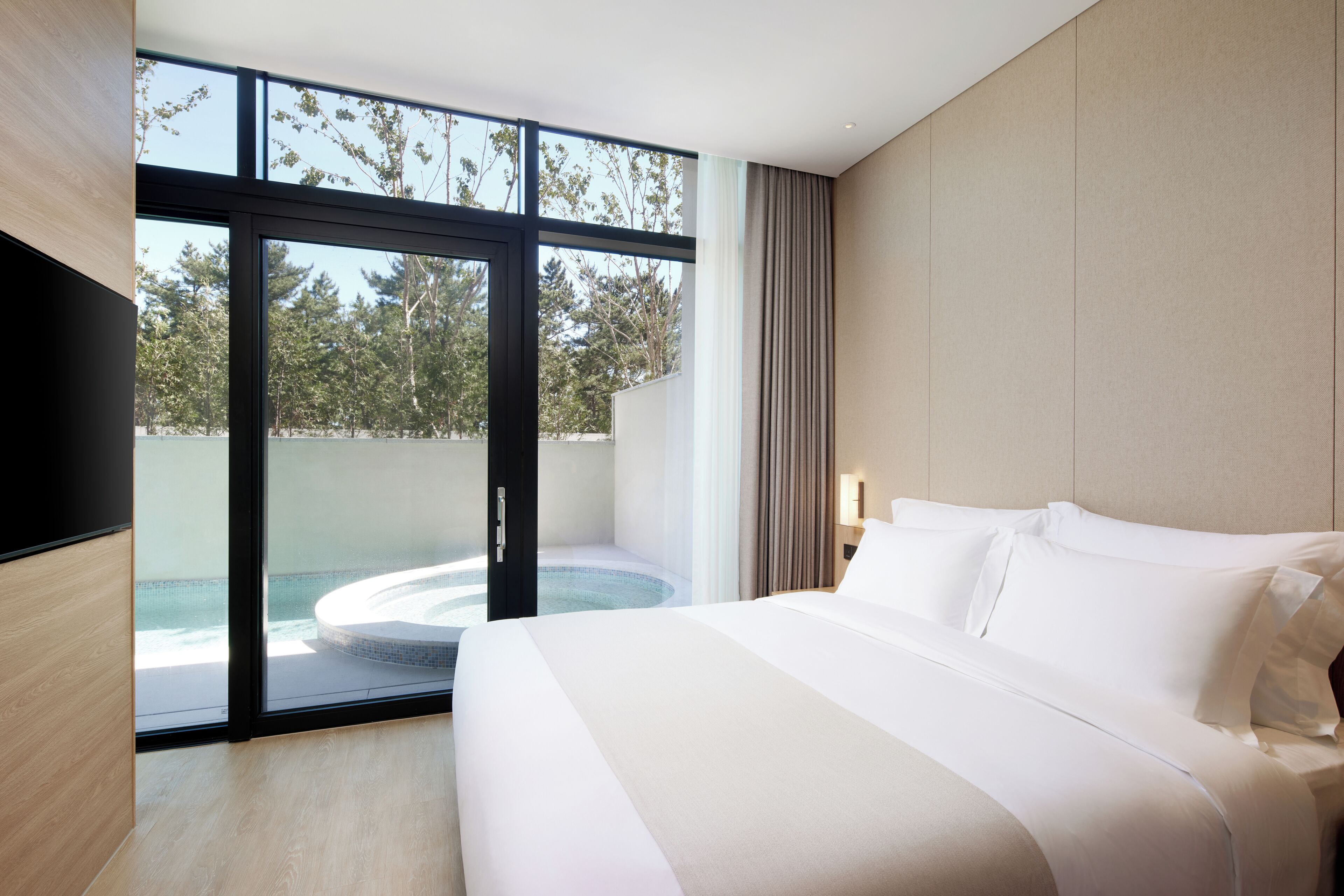 Ein modernes Hotelzimmer mit einem großen Bett, Blick auf eine Whirlpool-Anlage und einer Glastür, die zu einem Außenbereich führt.