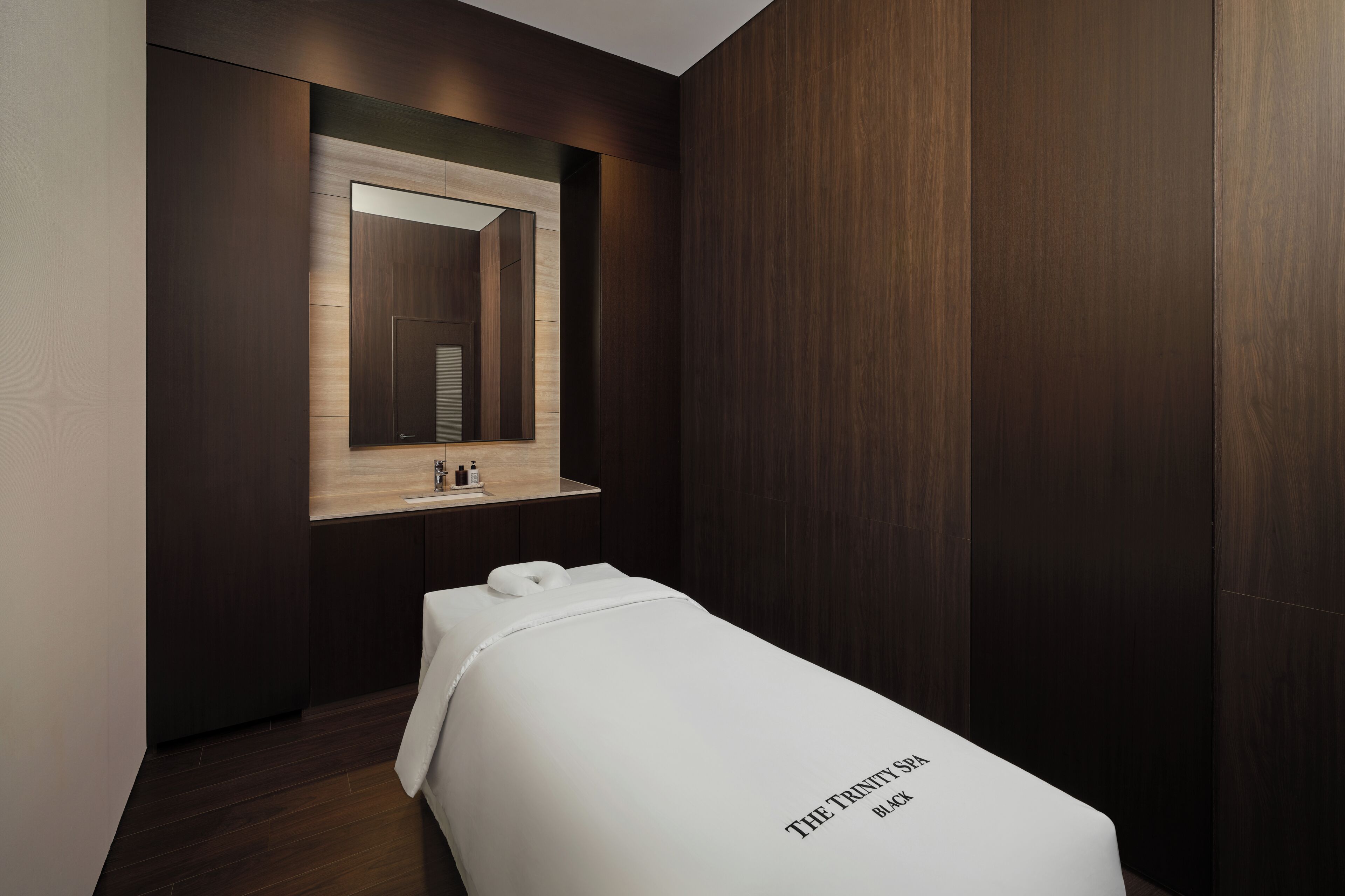 Un baño moderno con detalles en madera oscura, un espejo sobre un lavamanos y una toalla blanca sobre un banco.