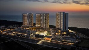 A high-rise hotel complex with multiple buildings, a well-lit parking area, and a view of the sea at dusk. - Shillamonogram Gangneung Residence (Gangneung)