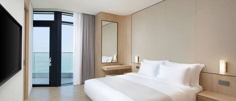 Habitación de hotel moderna con una cama grande, una mesita de noche, un espejo y vista al mar a través de un ventanal.