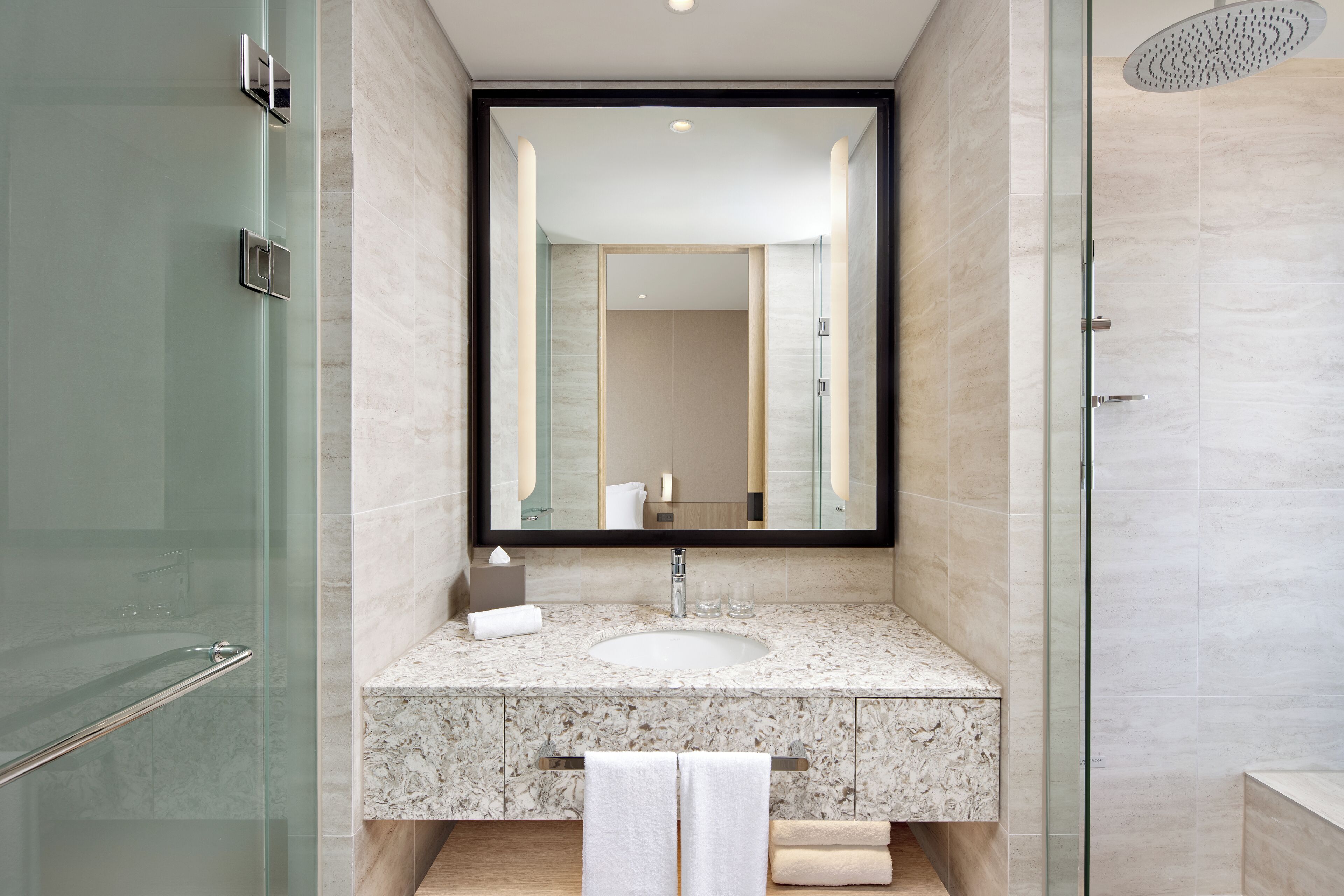 Un baño moderno con cabina de ducha de vidrio, lavamanos de mármol y un espejo grande.