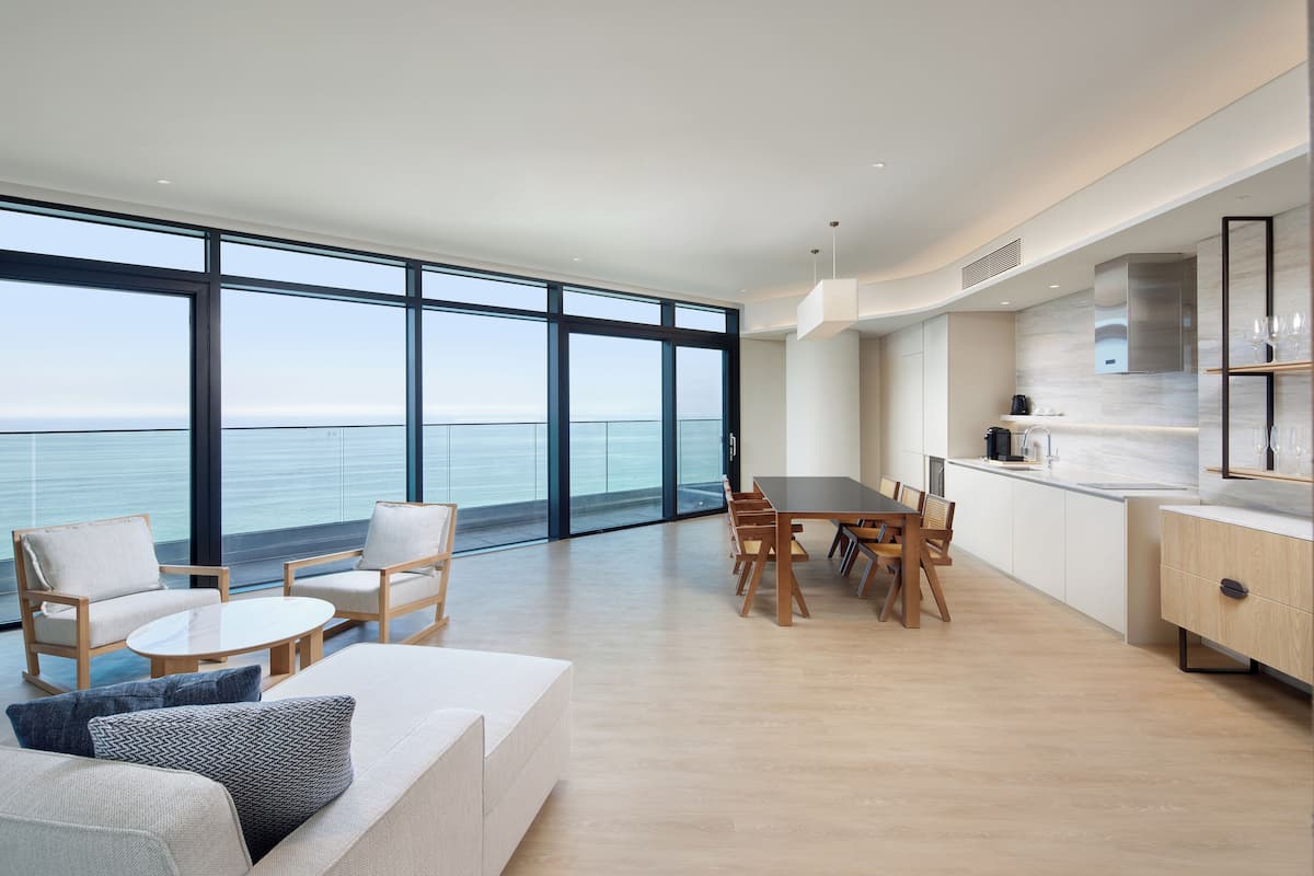 Ein modernes Wohnzimmer mit großem Fenster, Essbereich und einer Küche mit Meerblick.