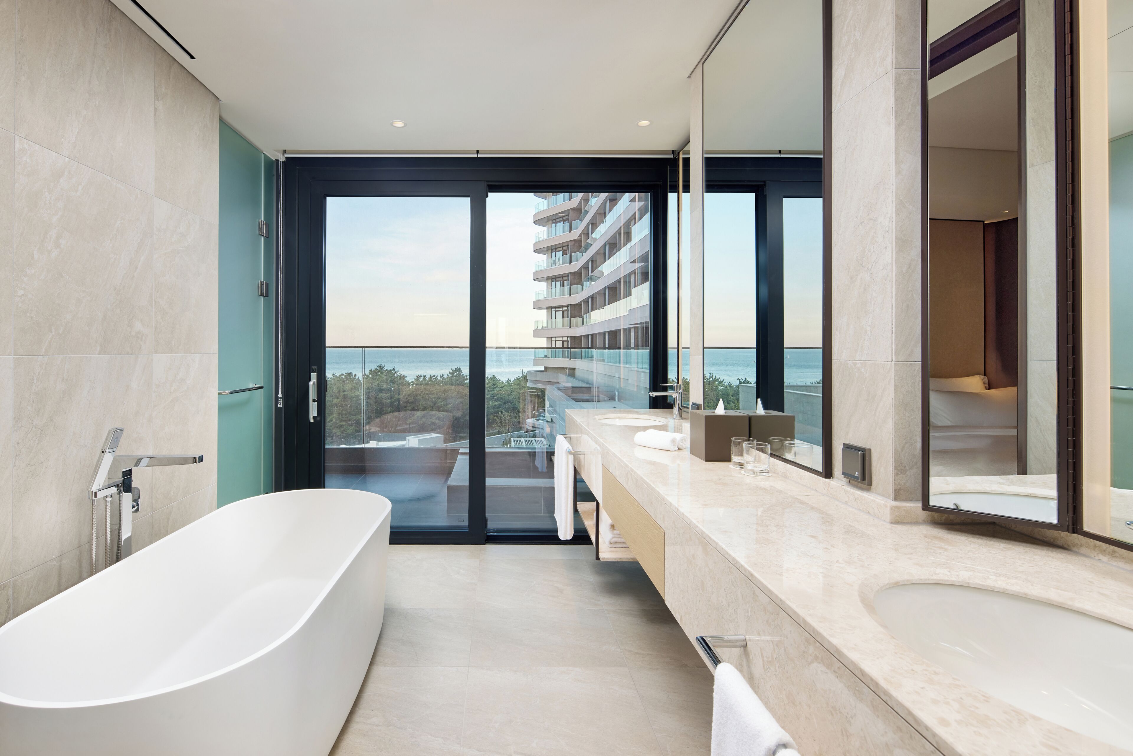 Un baño moderno con bañera, un espejo grande y vista a un edificio a través de una puerta de cristal.