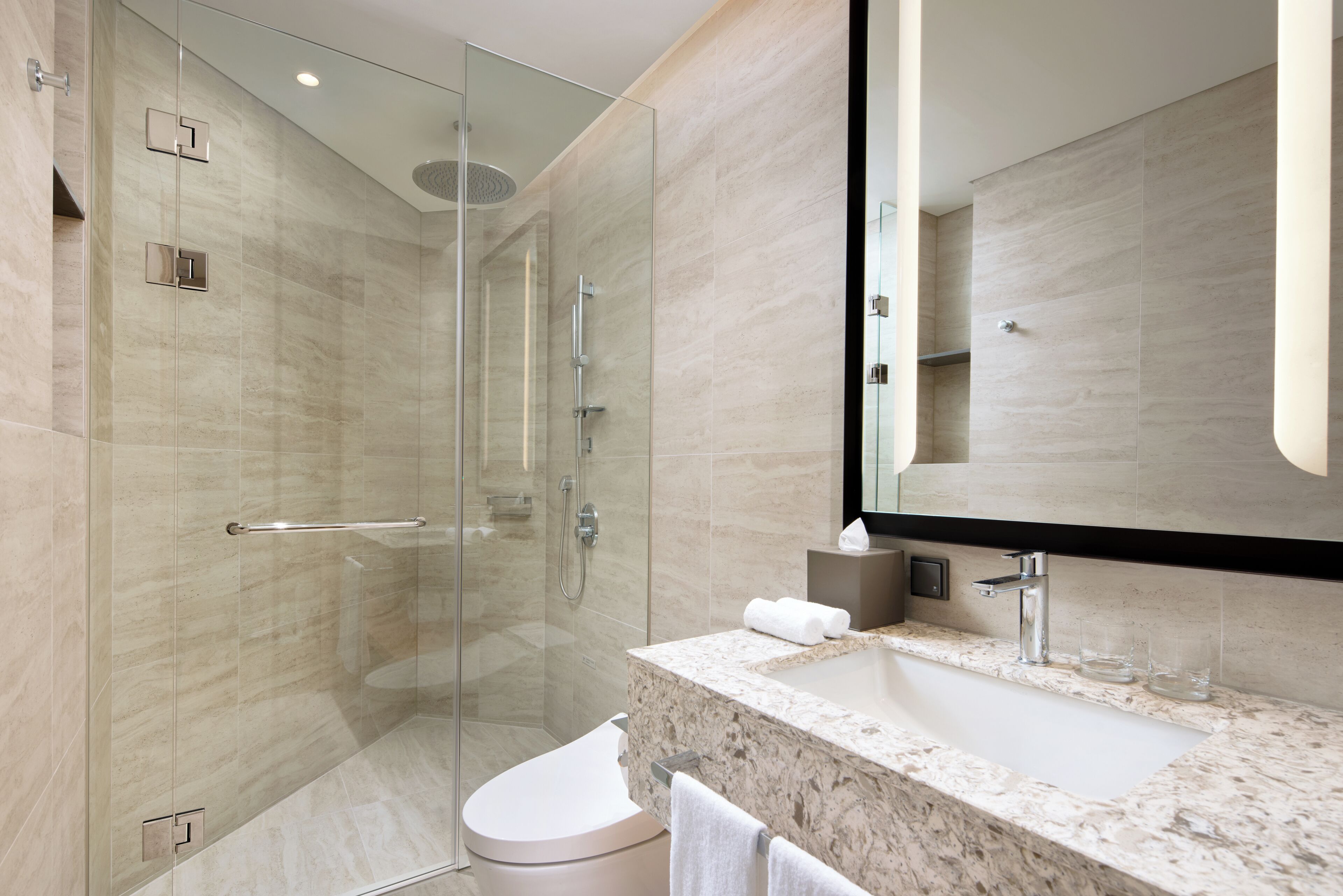 A modern bathroom with a glass-enclosed shower, a marble sink, and a large mirror.