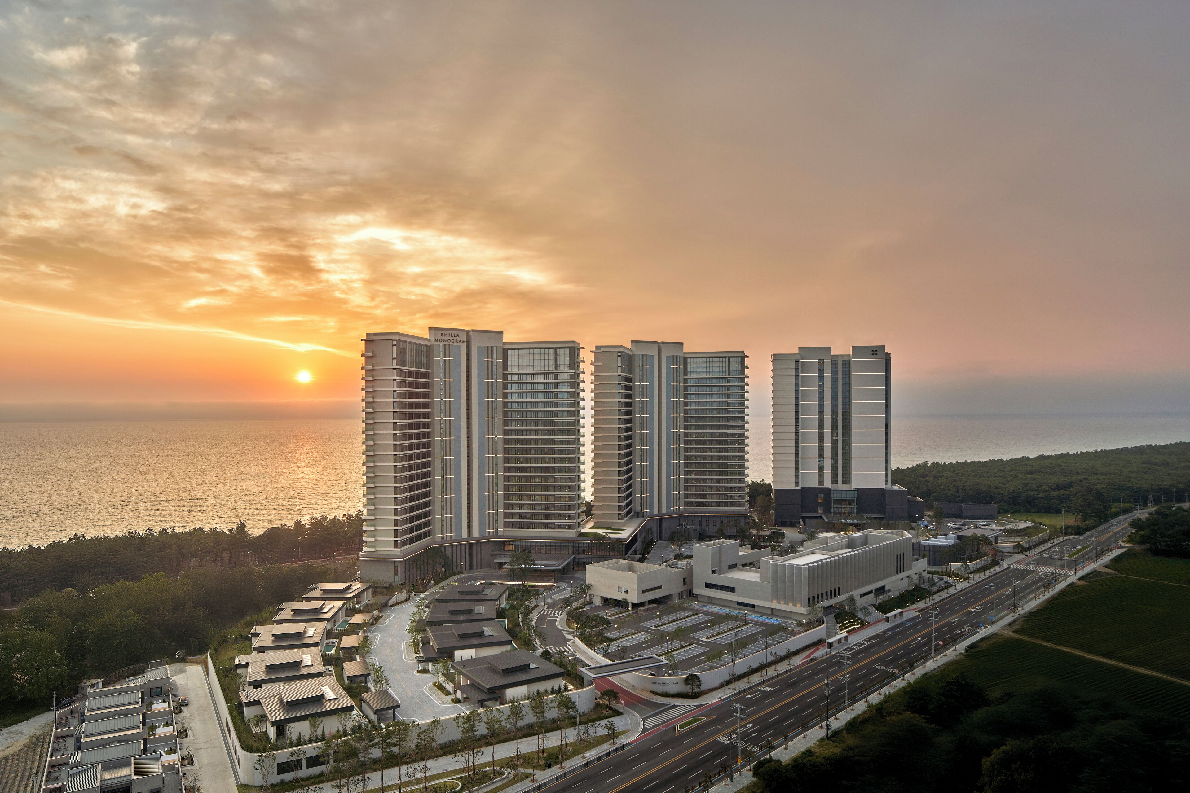 A high-rise building complex with multiple residential towers, a parking area, and a road leading to the sea.