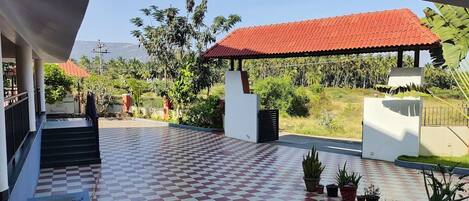 A checkered floor with potted plants, a covered area with a red roof, and a view of a lush landscape with trees and a mountain in the distance.
