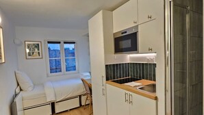 A compact kitchen with a microwave, sink, and wooden countertop. There is a window with a view of trees and a sofa with a chair in the adjacent living area. - Emily in Paris - Panthéon - Luxembourg - Studio (Paris)