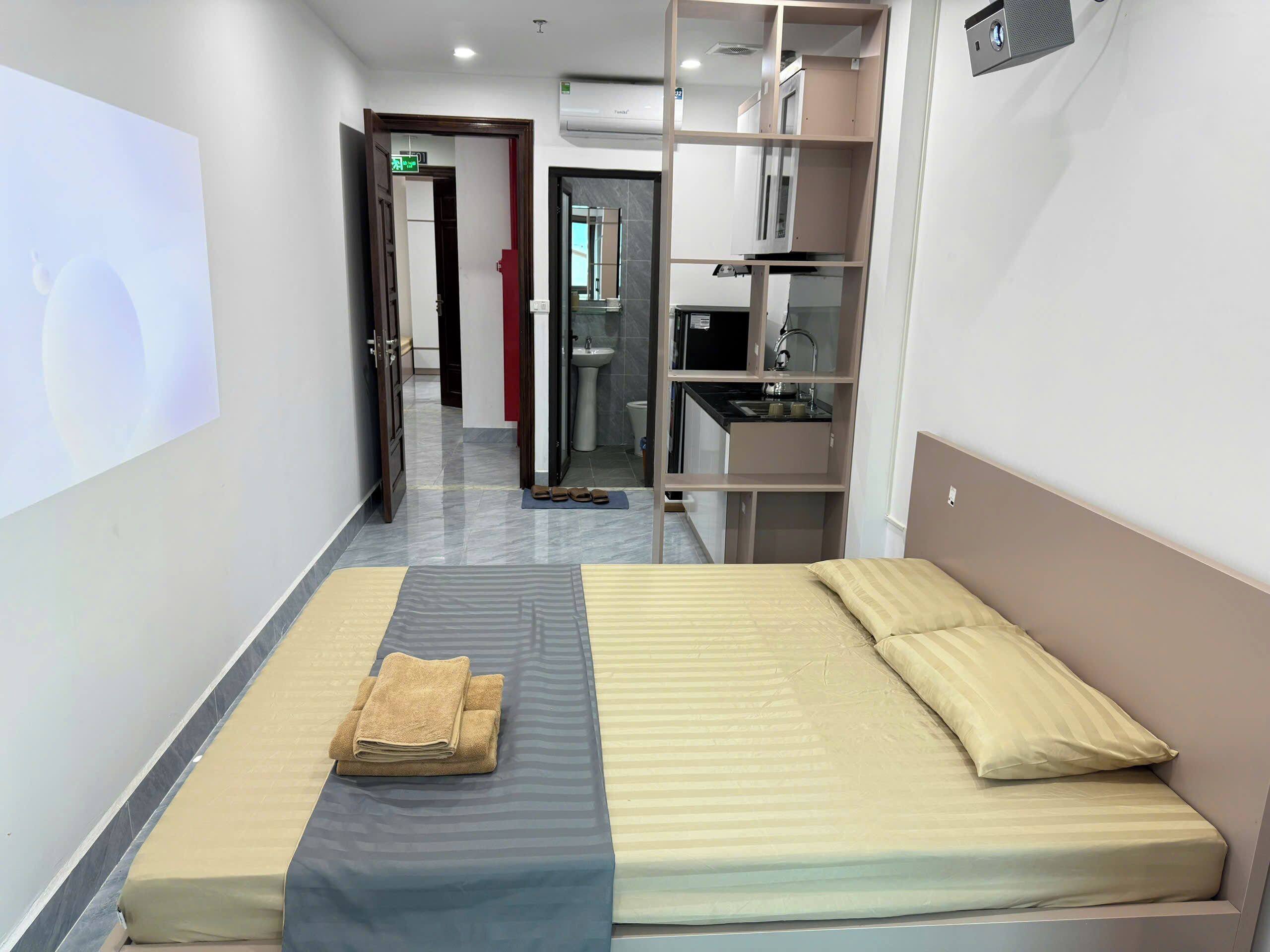 A hotel room with a bed, a small desk, a mirror, and a bathroom visible through an open door.