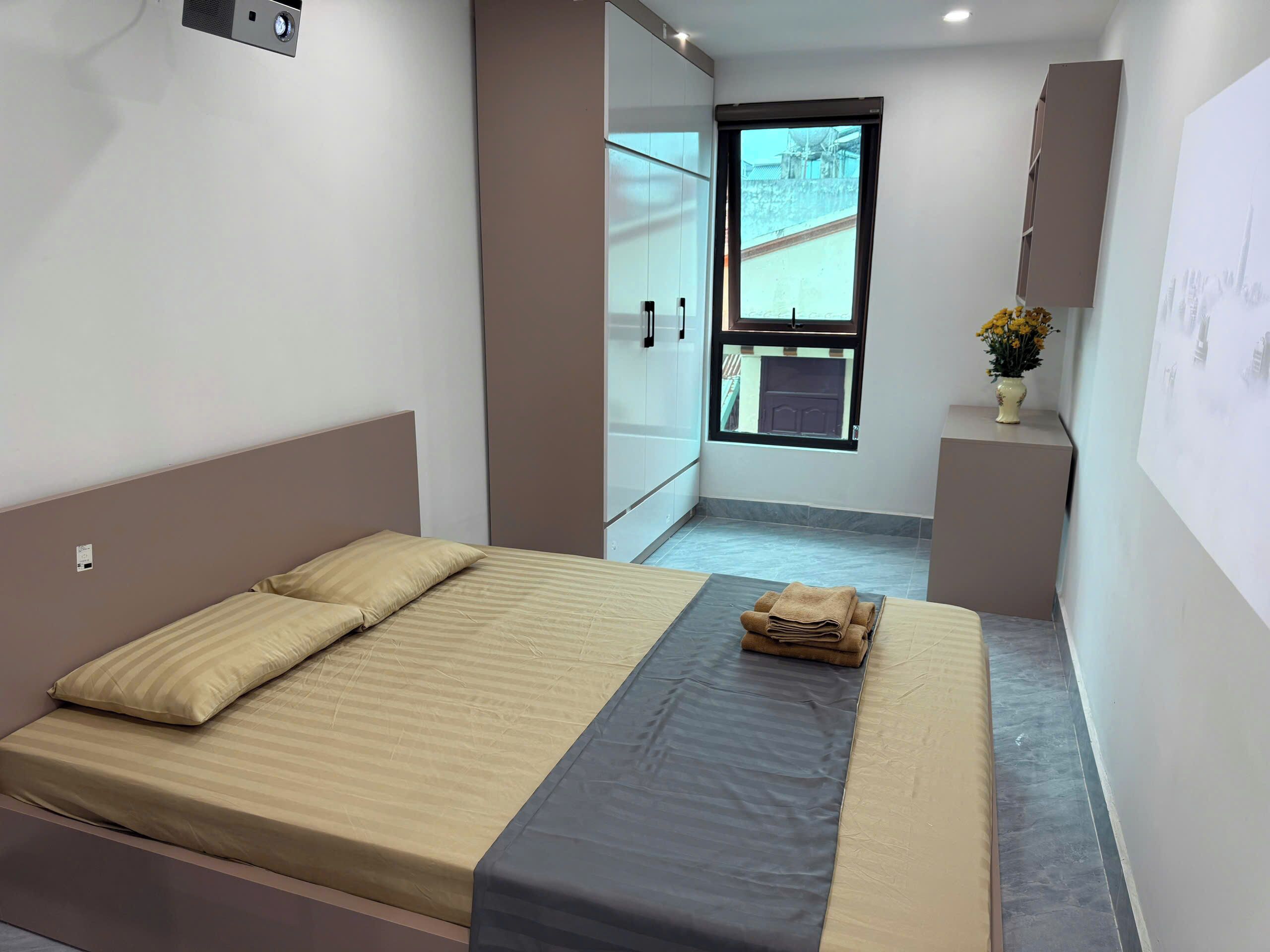A bedroom with a bed, a window, and a small table with a vase of flowers.
