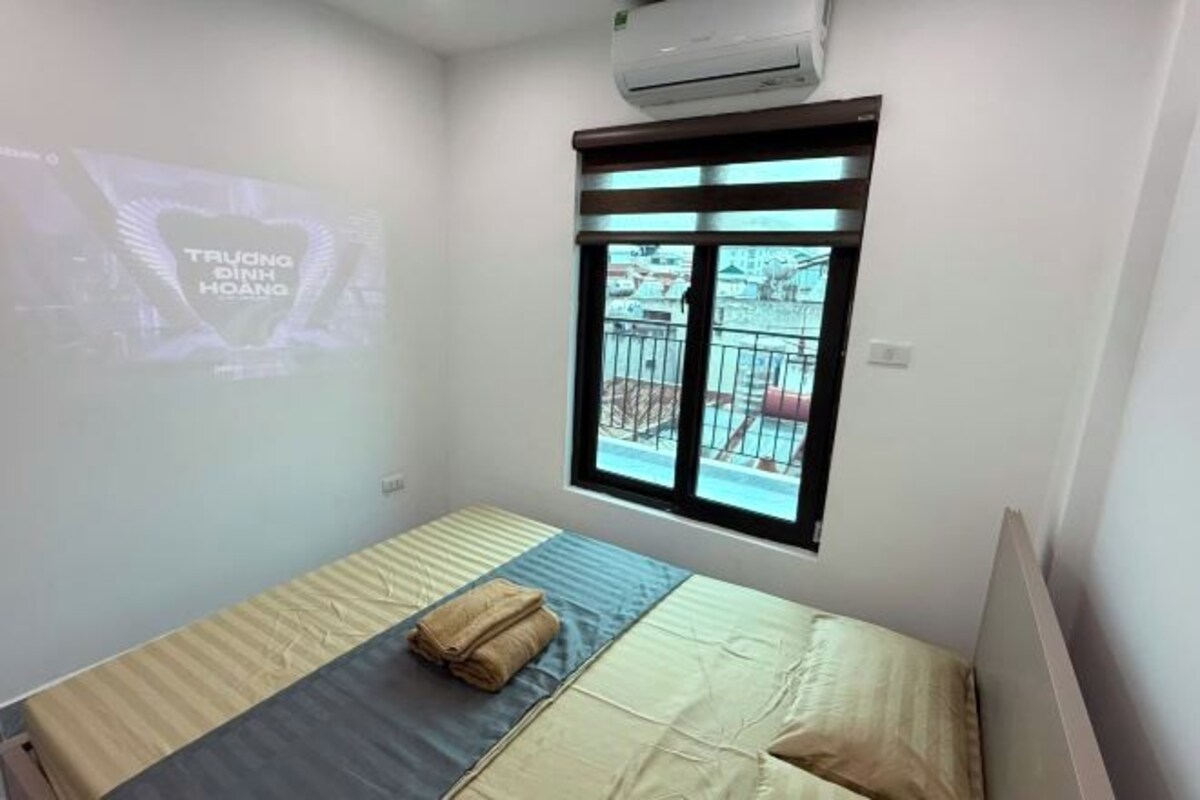 A small, clean room with a bed, a window with a view, and an air conditioning unit.
