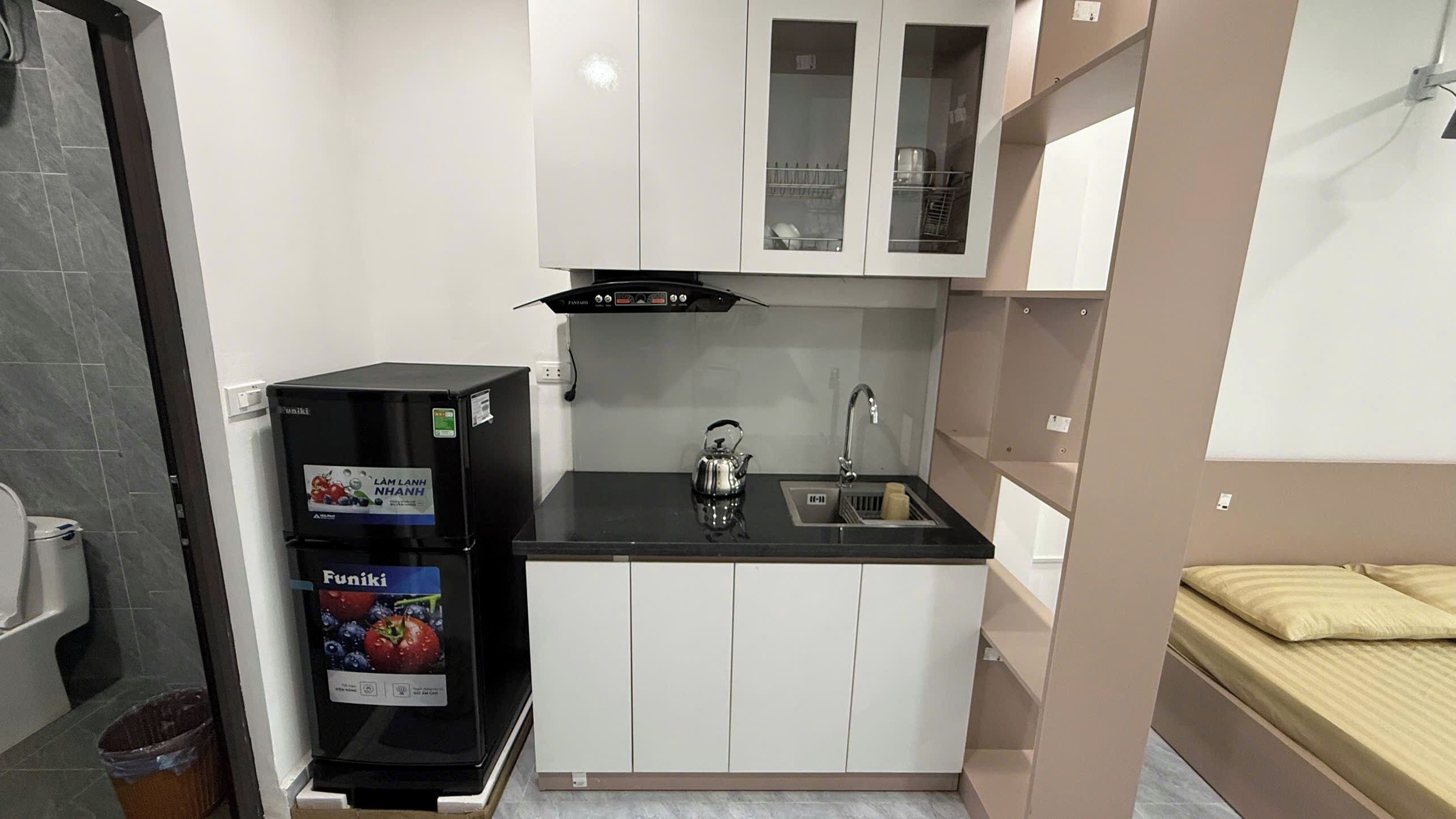 Eine kleine Küche mit einem schwarzen Kühlschrank, einem Wasserkocher und weißen Schränken.