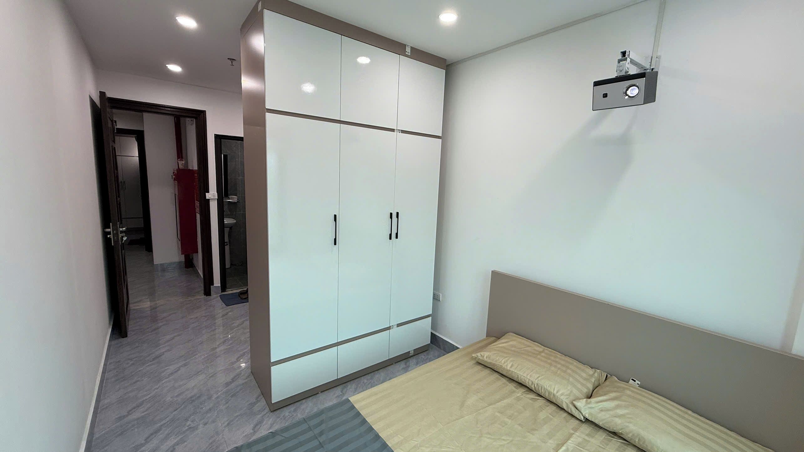 Un dormitorio con cama, armario y proyector instalado en el techo.