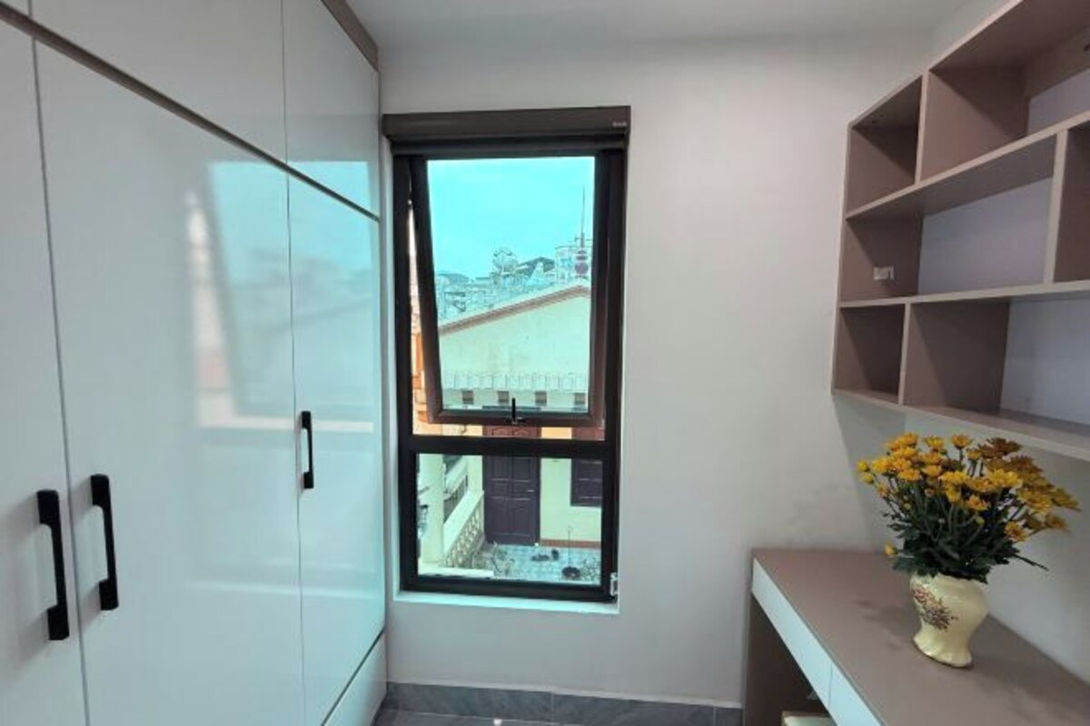 A modern bathroom with a window, a white cabinet, and a shelf with a vase of flowers.