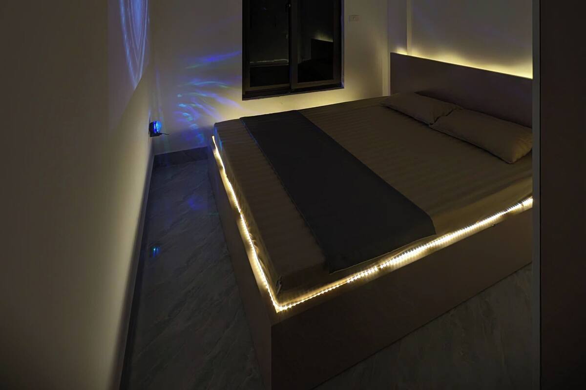 Un dormitorio moderno con cama, ventana, equipo de aire acondicionado y proyector en el techo.