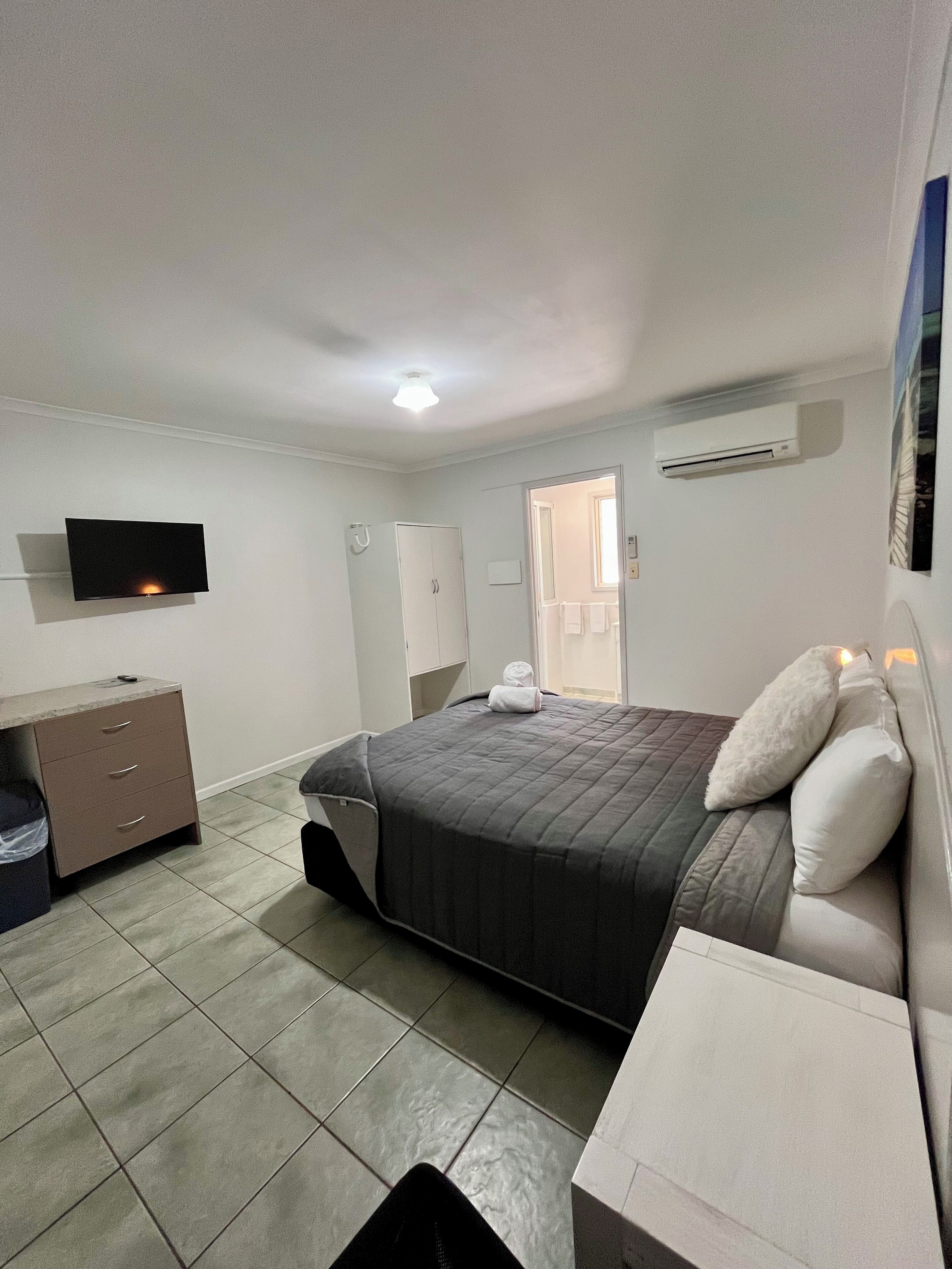 Habitación de hotel con cama, escritorio, televisor, armario y aire acondicionado.
