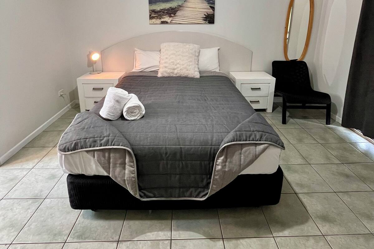 A bedroom with a bed, a nightstand, a chair, a mirror, and a painting of a beach.