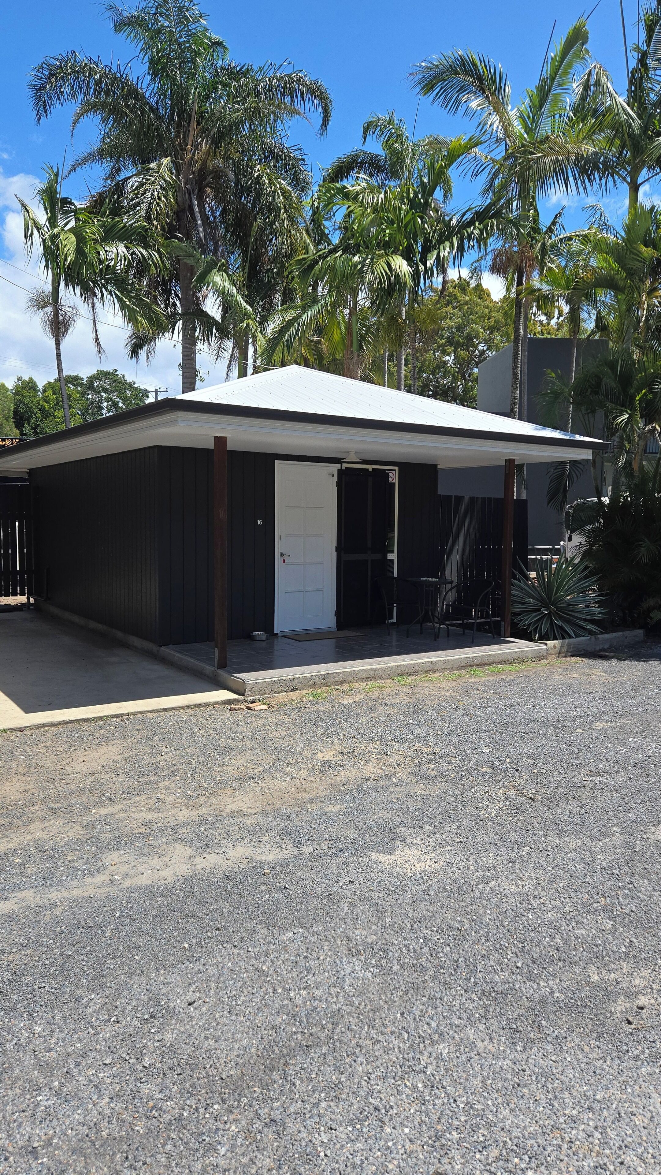 A single-story building with a flat roof, a covered porch area, and a gravel driveway.