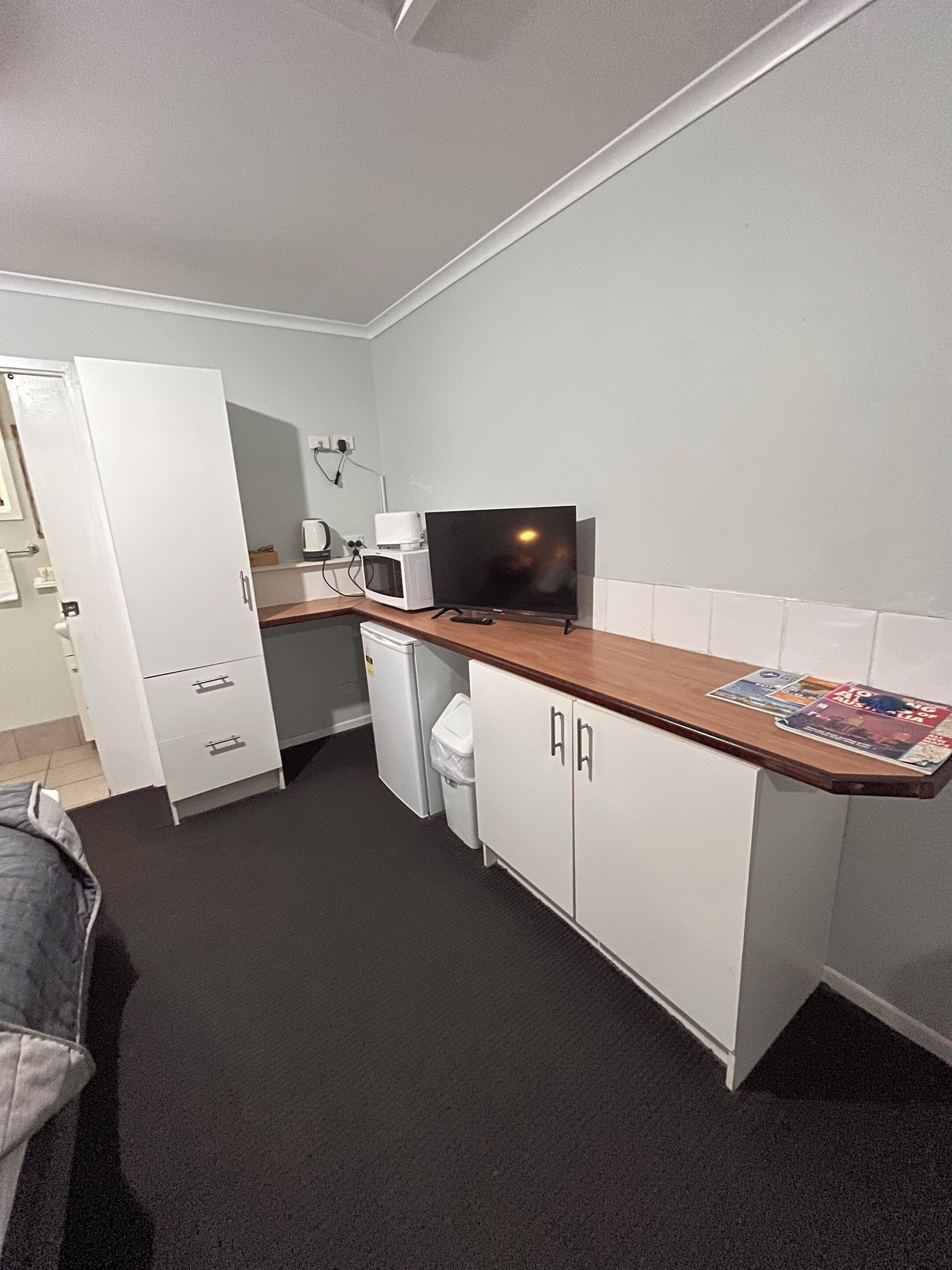 A compact kitchen with white cabinets, a microwave, a small refrigerator, and a television on a wooden countertop.
