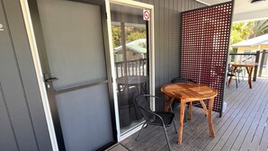 A covered outdoor area with a sliding glass door, a wooden table and chairs, and a red lattice partition. - Agnes palms motel (Agnes Water)