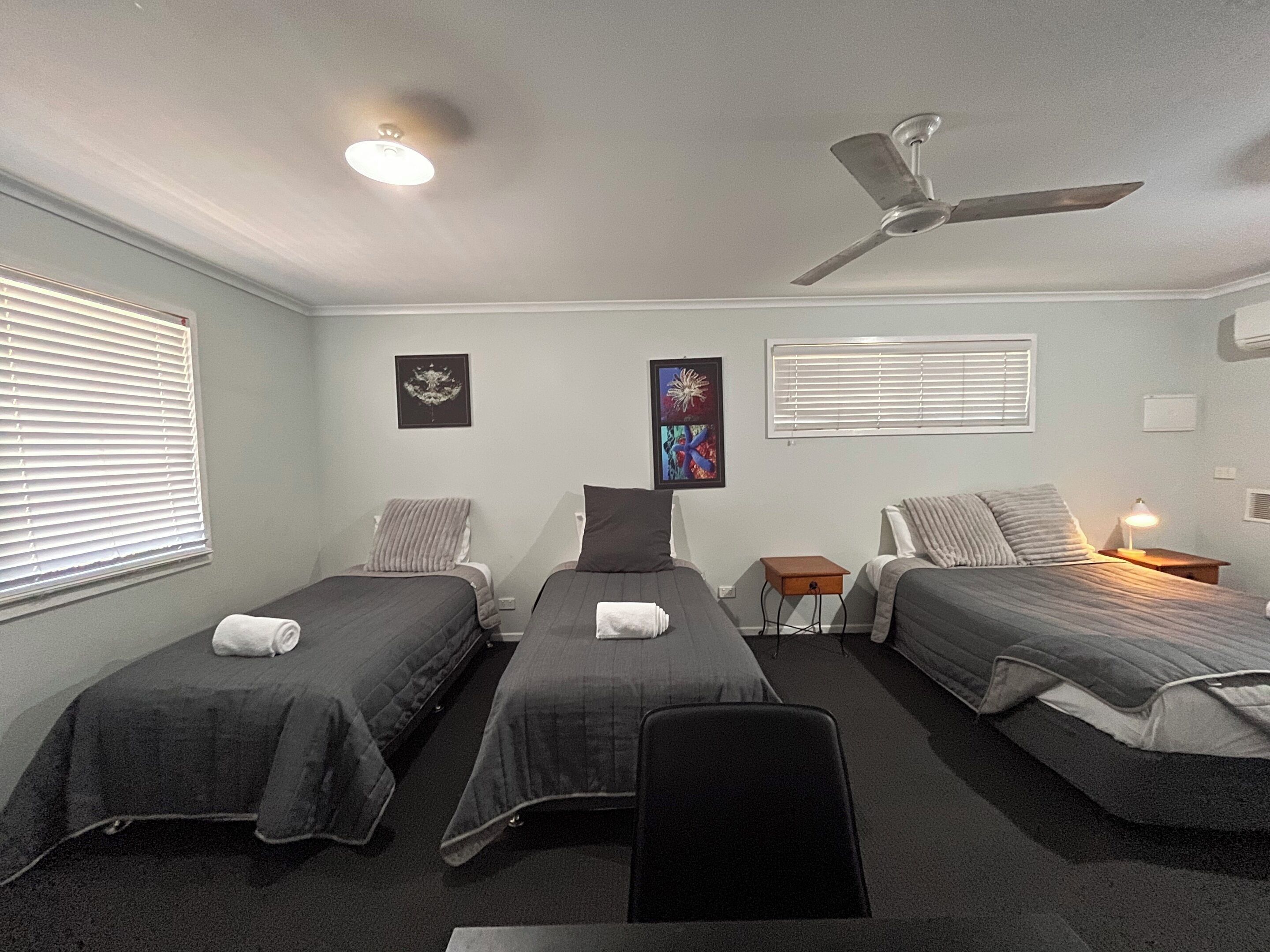 Una habitación con tres camas individuales, un ventilador de techo y dos lámparas fijadas a la pared.