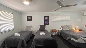 Una habitación con tres camas individuales, un ventilador de techo y dos lámparas fijadas a la pared.
