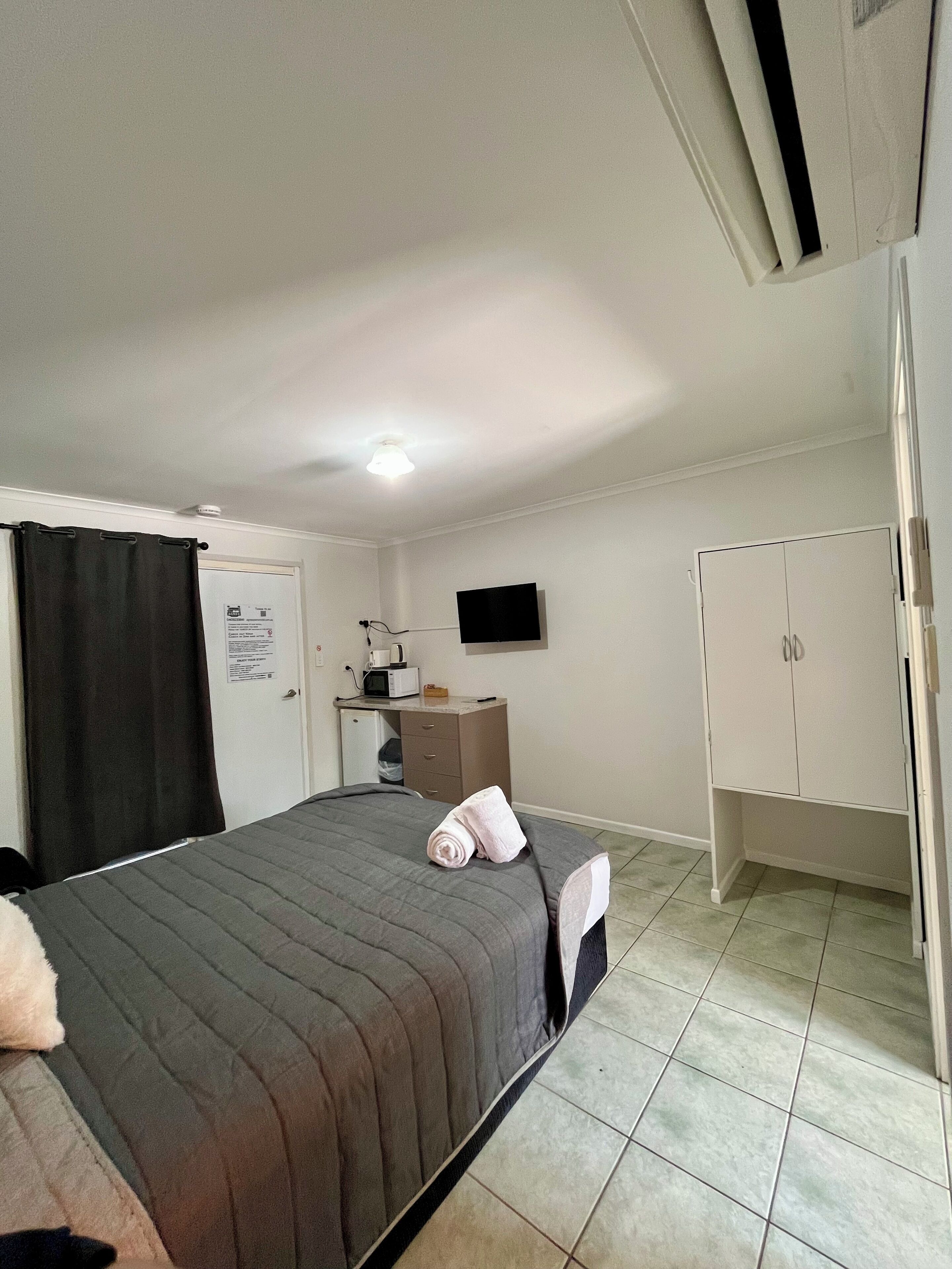 Una habitación de hotel con una cama, un escritorio con computadora, un televisor y un armario.