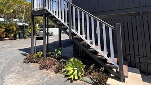 A modern building with a grey exterior, a wooden staircase with white railings, and a covered outdoor area with plants. - Agnes palms motel (Agnes Water)
